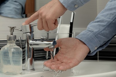 Man using water tap to wash hands in bathroom, closeup