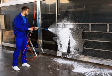 Worker cleaning auto mats with high pressure foam jet at car wash