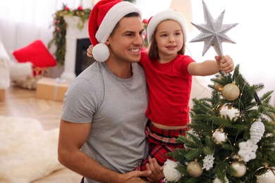 Photo of Father and little daughter decorating Christmas tree with star topper in room