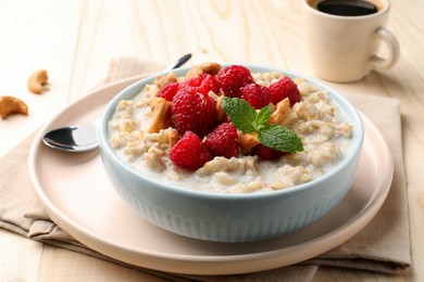 Photo of Bowl with tasty oatmeal porridge with nuts and raspberries on table, closeup. Healthy meal