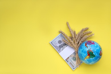 Import and export concept. Globe, ears of wheat and money on yellow background, flat lay with space for text