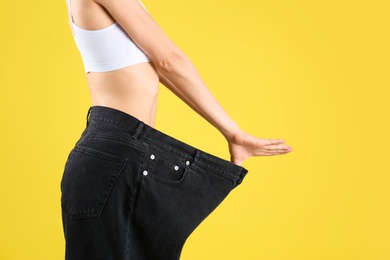 Young slim woman wearing oversized jeans on yellow background, closeup