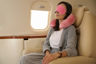 Young woman with travel pillow and mask sleeping in airplane during flight