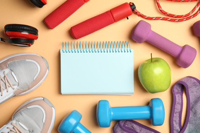 Photo of Flat lay composition with fitness equipment, notebook and apple on orange background, space for text
