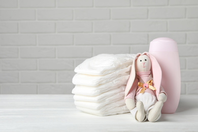 Baby diapers, toy bunny and bottle on wooden table against white brick wall. Space for text