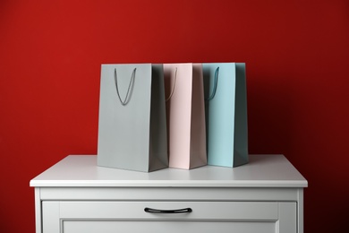 Paper shopping bags on white chest of drawers against red background