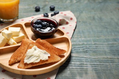 Tasty toasts with butter and blueberries on light blue wooden table, closeup. Space for text