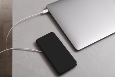 Smartphone with wireless charger connected to laptop on light grey table, above view. space for text
