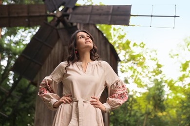 Photo of Beautiful woman wearing embroidered dress near old wooden mill in countryside. Ukrainian national clothes