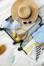 Photo of Open suitcase full of clothes, slippers and summer accessories on bed, flat lay