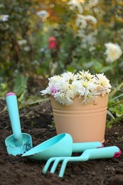 Photo of Gardening tools and bucket with flowers on ground in garden