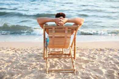 Young man relaxing in deck chair on beach near sea