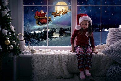 Cute little girl on window sill at home waiting for Santa Claus. Christmas celebration