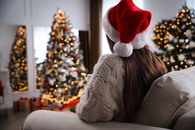 Beautiful young woman wearing Santa hat in room decorated for Christmas, back view