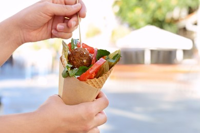 Woman eating wafer with falafel and vegetables outdoors, closeup. Space for text