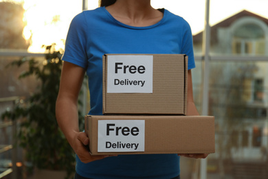Courier holding parcels with stickers Free Delivery indoors, closeup