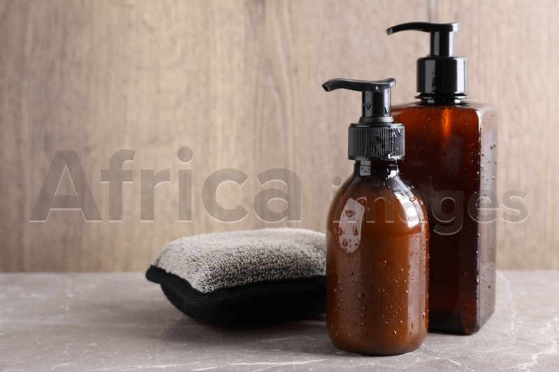 Photo of Dispenser bottles with water drops and bast wisp on beige marble table, space for text. Men's cosmetics