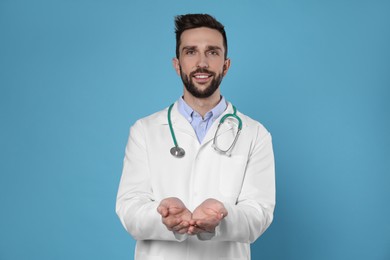 Doctor with stethoscope holding something on light blue background. Cardiology concept