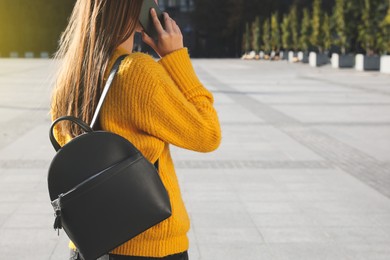 Young woman with stylish black backpack talking on phone outdoors, closeup. Space for text