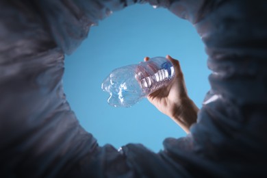 Bottom view of woman throwing plastic bottle into trash bin on light blue background, closeup