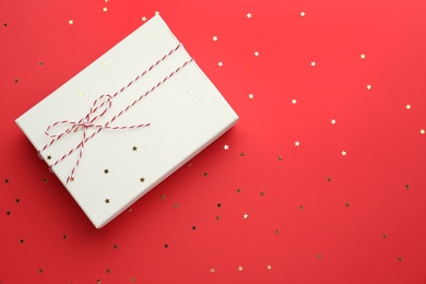 Gift box and confetti stars on red background, flat lay. Christmas celebration