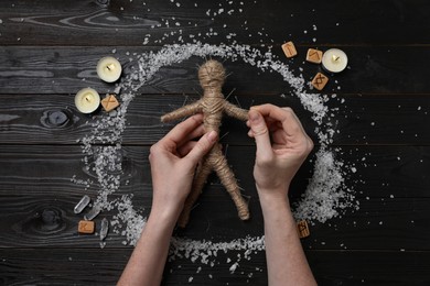 Woman stabbing voodoo doll with pins at wooden table, top view