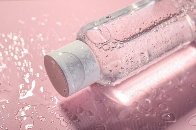 Wet bottle of micellar water on pink background, closeup