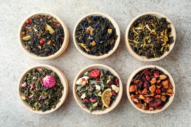 Photo of Different kinds of dry herbal tea in wooden bowls on light grey table, flat lay