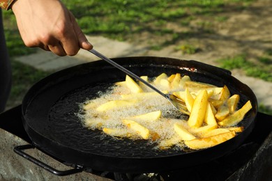 Man cooking delicious potato wedges on frying pan outdoors, closeup