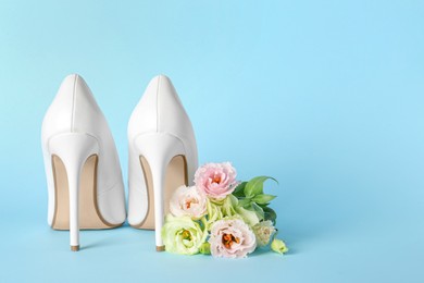 Stylish women's high heeled shoes and beautiful flowers on light blue background, space for text
