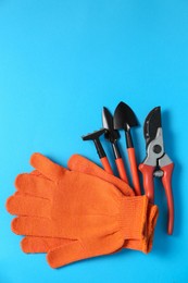 Gardening gloves and tools on light blue background, flat lay. Space for text