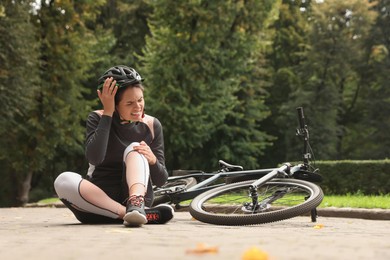 Young woman with injured knee near bicycle outdoors