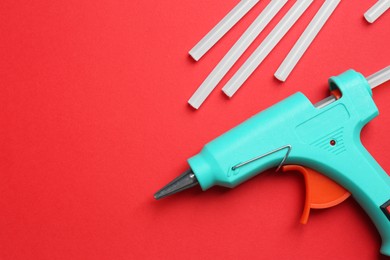 Turquoise glue gun and sticks on red background, flat lay. Space for text