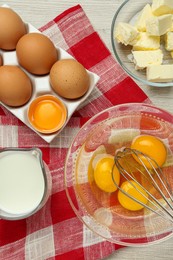Whisk, eggs in bowl, milk and butter on white wooden table, flat lay