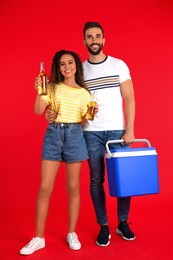 Happy couple with cool box and bottles of beer on red background