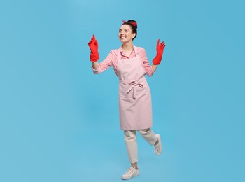 Housewife wearing rubber gloves on light blue background
