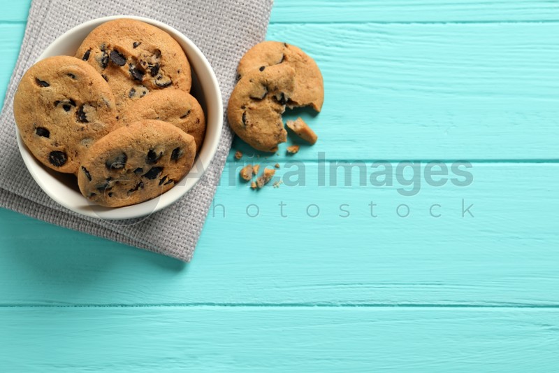 Bowl with many delicious chocolate chip cookies on turquoise wooden table, flat lay. Space for text