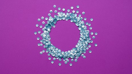 Circle made of silver sequins on purple background, top view