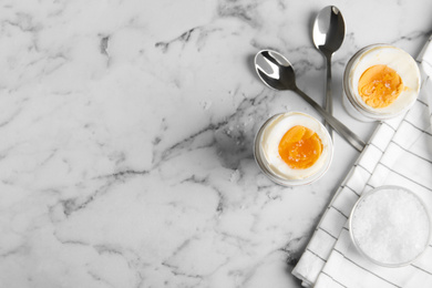 Tasty medium boiled eggs in ceramic holders on white marble table, flat lay. Space for text