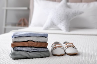 Stack of baby boy's clothes and shoes on bed at home, space for text
