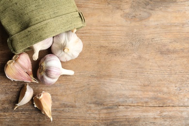 Fresh unpeeled garlic bulbs and sack on wooden table, flat lay with space for text. Organic product