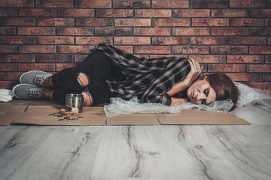 Poor homeless woman sleeping on floor near brick wall