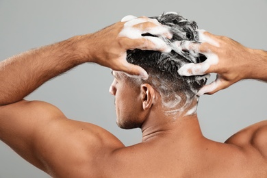 Handsome man washing hair on grey background, back view