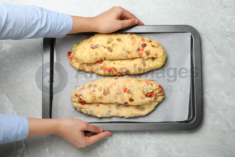 Woman holding baking tray with raw homemade Stollens at grey table, closeup. Traditional German Christmas bread