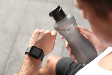 Man with bottle of water checking fitness tracker after training outdoors, closeup