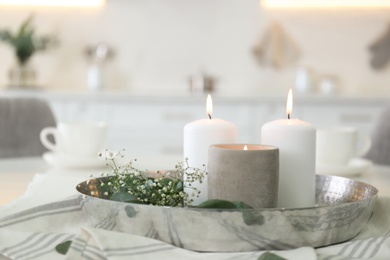 Photo of Beautiful eucalyptus branches, flowers and burning candles on napkin in kitchen. Interior element