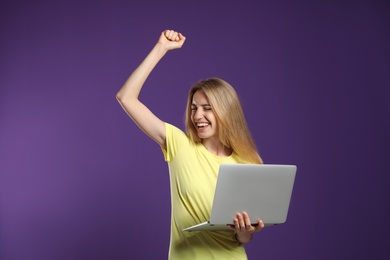 Portrait of emotional woman with modern laptop on purple background