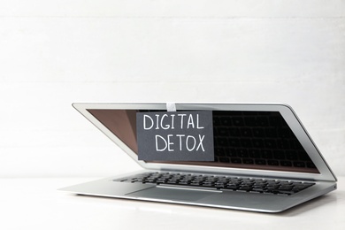 Laptop and paper with words DIGITAL DETOX on white wooden table