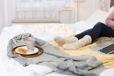 Woman with cup of hot drink and wafers on bed at home. Cozy winter
