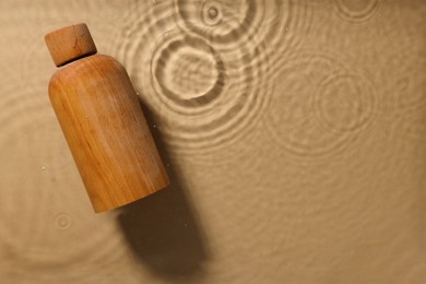 Photo of Wooden bottle of cosmetic product in water on beige background, top view. Space for text